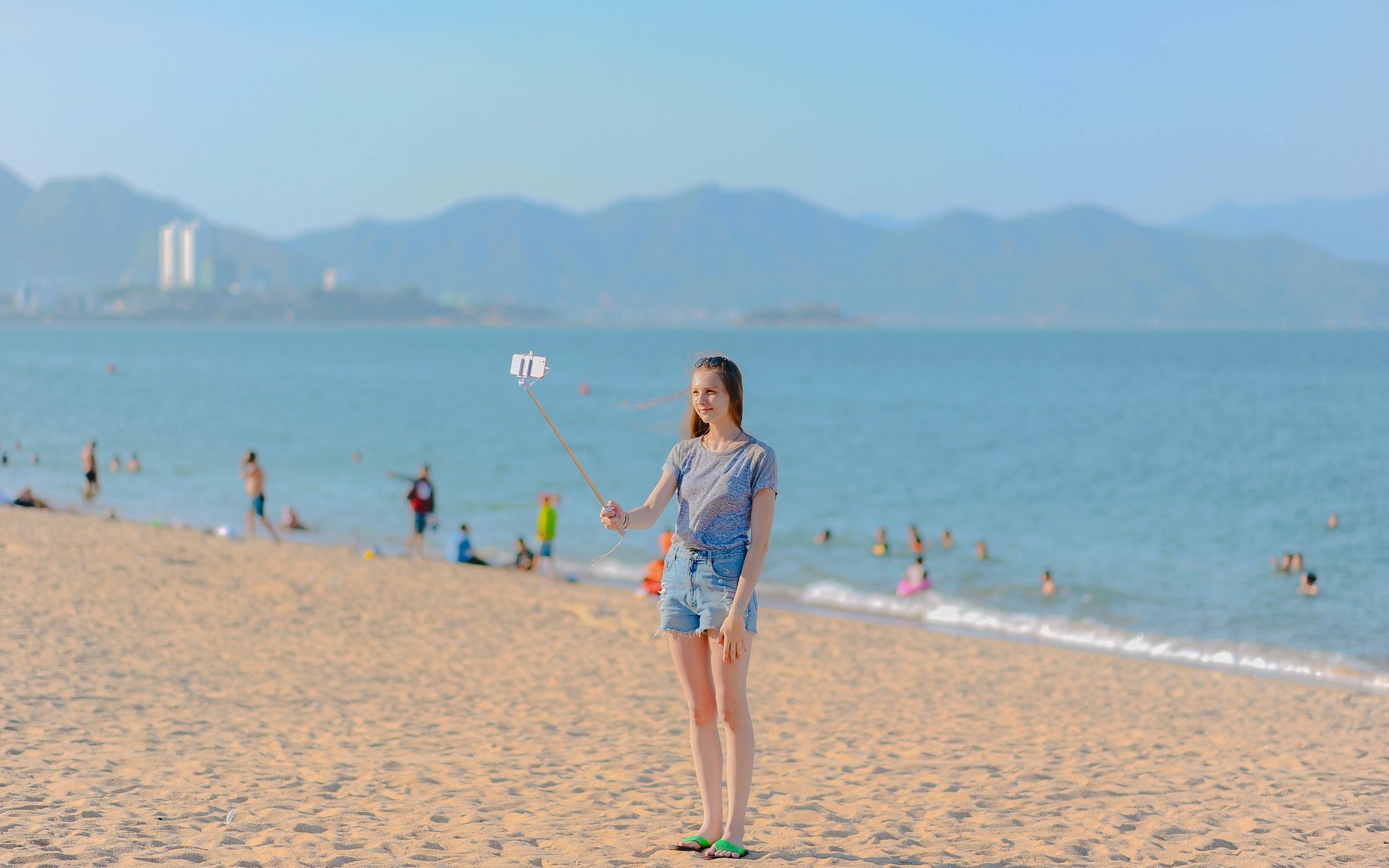 Woman standing on seashore taking selfie using monopod at 1213974